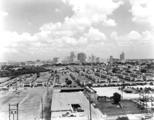 HCU campus skyline in black and white, warehouses and parking lots in foreground beneath a cloudy sky.