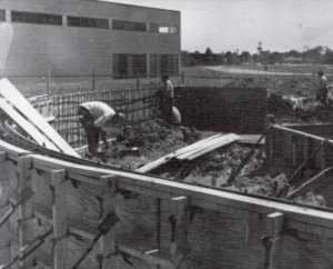 Workers pour concrete foundation on HCU campus for a building’s 60th Anniversary in this black and white historic construction scene.
