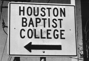Black and white sign directs with a left-pointing arrow under Houston Christian University text on HCU campus.