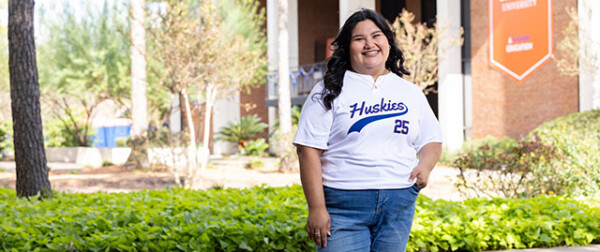 Woman in Huskies 25 jersey smiles outdoors on HCU campus, enjoying student life near vibrant university landmarks.