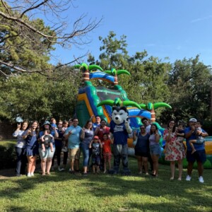 Students and a wolf mascot gather on HCU campus by an inflatable water slide during a sunny outdoor event.