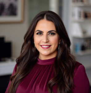 A woman in a maroon blouse smiles inside a modern office, preparing to lead a HealthCare Lunch & Learn this spring semester.