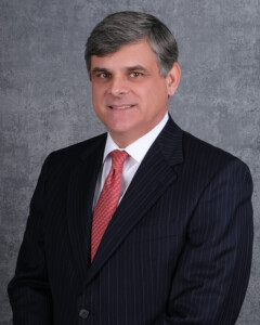 Business professional in pinstripe suit and red tie stands before gray textured wall at academic conference.