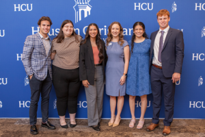 Six business alumni smile in front of a blue Dunham Houston Christian University backdrop, dressed business casual.