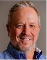 Smiling middle-aged man with gray hair in blue shirt at academic mentoring event on Houston Christian University campus.