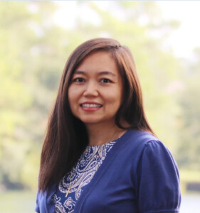 Smiling woman with long dark hair in a blue patterned top outdoors at Together We Rise on HCU campus.