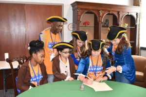 young children participate in a mock signing of the constitution wearing historical costumes