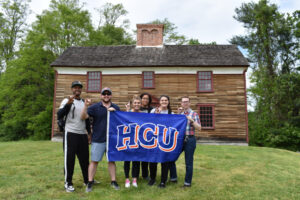 students stand outside of an old historical building in Boston holding an HCU flag