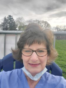 Terri Kimble with short brown hair and glasses in scrubs sits outside HCU campus field hospital on a cloudy day.
