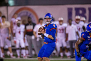 HCU quarterback in blue uniform winds up to throw on campus field, highlighting student athletics during a shifting season.
