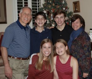 The Tim Mavergeorge family of six smiles near a decorated Christmas tree in their cozy living room, celebrating together.