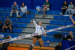 A Houston Christian University volleyball player in a white jersey jumps to spike the ball, highlighting athletic excellence.
