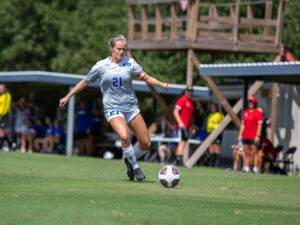 Soccer player in white uniform sprints for the ball on HCU campus field, showcasing athletics and changing seasons.