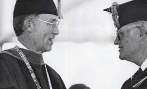 Two men in academic regalia exchanging smiles at Houston Christian University’s 60th Anniversary graduation ceremony.