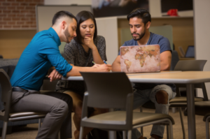 Students collaborating on Mission Metacognition, gathered around a laptop and notes in a contemporary study area.