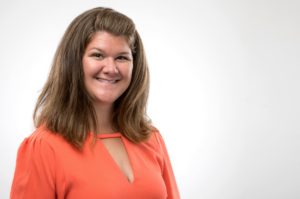 Mary Catherine Harmon in orange top with long brown hair, representing Houston Youth, stands before plain white indoor background.