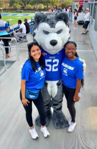 Andrea Ramirez and a friend in blue Huskies shirts smile with the husky mascot during a Senior Year Experience on HCU campus.