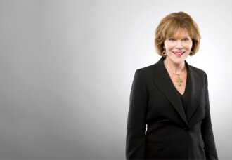 Woman in black suit smiles before a light grey backdrop, honoring Dr. Barbara J. Elliott's legacy at Houston Christian University.