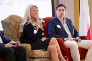 A faculty member discusses real estate closing into a mic alongside a colleague during an academic panel in an indoor lecture hall.