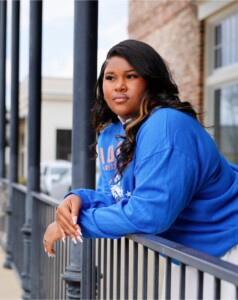 Student in a blue sweatshirt leans on a black railing at HCU campus, gazing thoughtfully across the outdoor grounds.