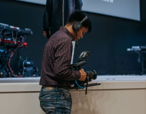 Film student wearing headphones operates a stabilizer in a low-lit studio, focusing on innovative media production techniques.