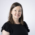 Smiling woman in black top celebrates HCU Apologetics, framed by a light gray background for academic engagement.