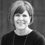 Woman with short hair, dark top, and necklace smiling for HCU Apologetics, blurred background enhances focus on her expression.