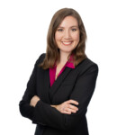 Woman in black blazer and magenta shirt stands with arms crossed, smiling, ready for Apologetics Day at Houston Christian University.