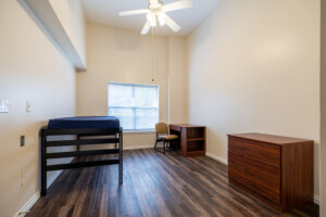 University Place dorm room with lofted bed, desk, chair, dresser, and window blinds in a student residential setting.