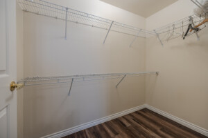 Walk-in closet with beige walls, wire shelving, and dark wood flooring inside a residence hall on Houston Christian University campus.