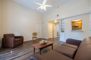 Cozy living room with brown seating, coffee table, ceiling fan, wood floors, and neutral walls in a university housing setting.