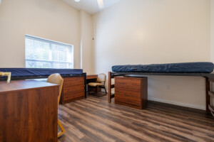 Dorm room with two elevated beds, desks, chairs, dressers, and window blinds in a University Place residence hall.