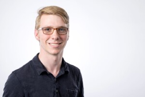 Smiling student in dark shirt and glasses, embodying welcoming spirit of Residence Life, set against a plain white background.