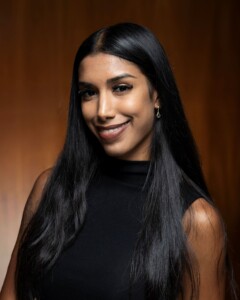 Smiling woman with long black hair in a black sleeveless top, expressing enthusiasm for human resource management academics.