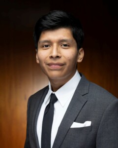 Young man in a gray suit and black tie smiles slightly during a business seminar, reflecting strong HRM principles.