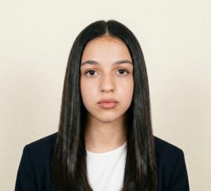 A student with long straight dark hair in a white top and dark blazer demonstrates professionalism in an academic setting.