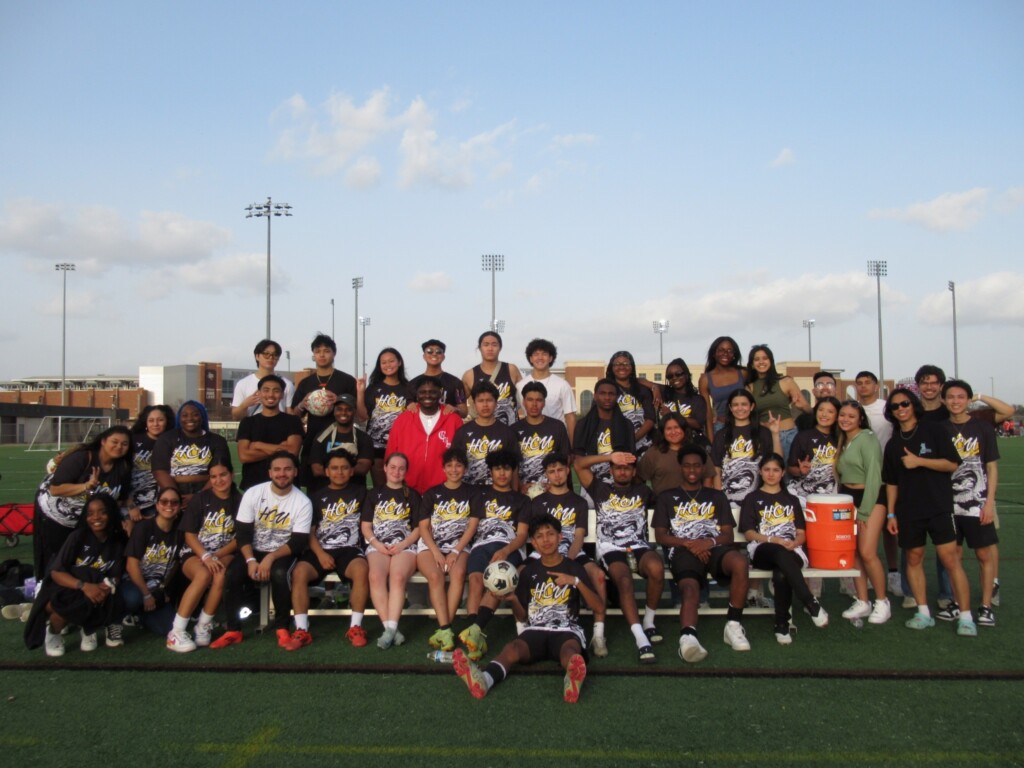 Filipino students in matching shirts gather on HCU campus soccer field, smiling together on a sunny day.