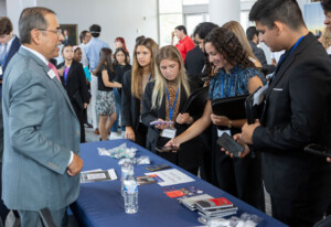 Students engage with a recruiter at an indoor career fair table, reviewing informational brochures and networking opportunities.