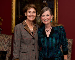 Two women smiling inside a campus coffee shop, standing together by a painting next to a red accent wall.