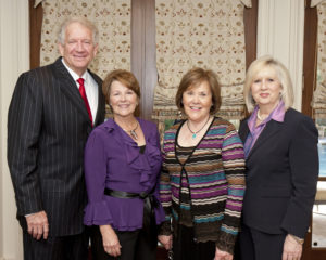 Business professionals gather by a window, sharing coffee during an academic networking event on campus.