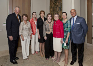 Group of eight adults dressed formally at a Silver Teas event, posing and smiling together inside an academic event space.