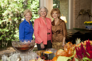 Three older women enjoy punch and snacks together at a campus social event in an HCU meeting space.