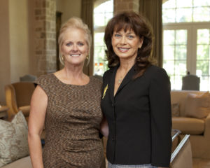 Two women in a sunlit lounge discuss Guild Fall Coffees, surrounded by cozy couches and expansive windows in an academic setting.