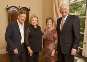 Four smiling adults in formal attire pose together at a Guild Fall Coffees event, standing in a warmly lit gathering space.