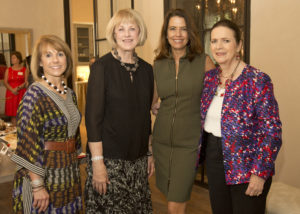 Four women in business casual attire share a smile at a Guild Fall Coffees event inside an academic building during a social gathering.