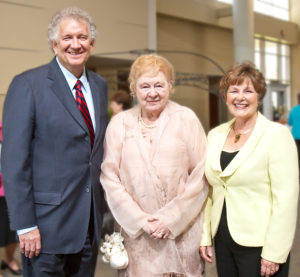 Three older adults in formal wear share smiles at a Silver Teas event indoors, participating in a university alumni gathering.