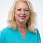 Cheryl Kaminski with blonde, wavy hair, turquoise blouse, and gold necklaces poses by Dr. Robert Sloan, white background.