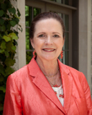 On the HCU campus, a Alford Draper Ruth with brown hair in a coral blazer stands outside near lush greenery and a campus building.