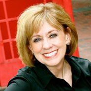 Woman with short light brown hair in black top, smiling at a festive luncheon with red background during a campus event.