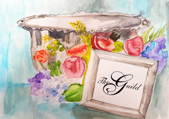 Silver vase of colorful flowers beside a framed sign reading The Guild in elegant script at a campus event display table.
